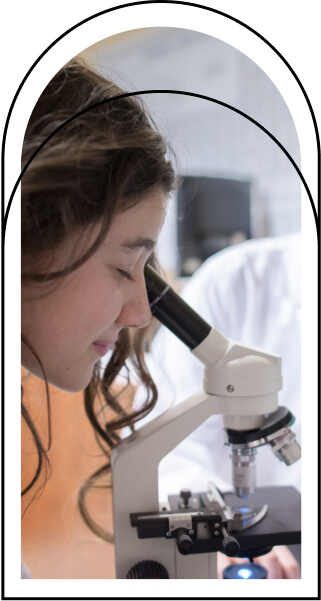 Étudiante utilisant un microscope, exploration scientifique, blouse blanche, concentration sur l'observation, apprentissage pratique en classe, environnement éducatif, découverte des sciences, implication académique, ambiance studieuse et motivante.