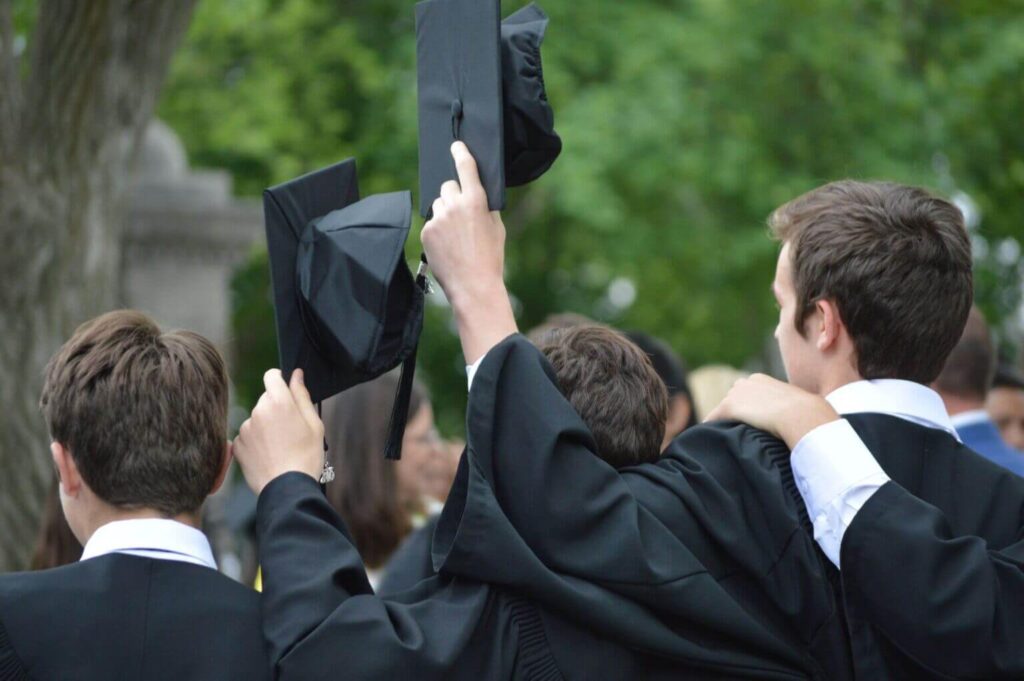 Étudiants en toges de remise de diplômes, chapeaux en l'air, célébration de la réussite scolaire, extérieur verdoyant, camaraderie et accomplissement.