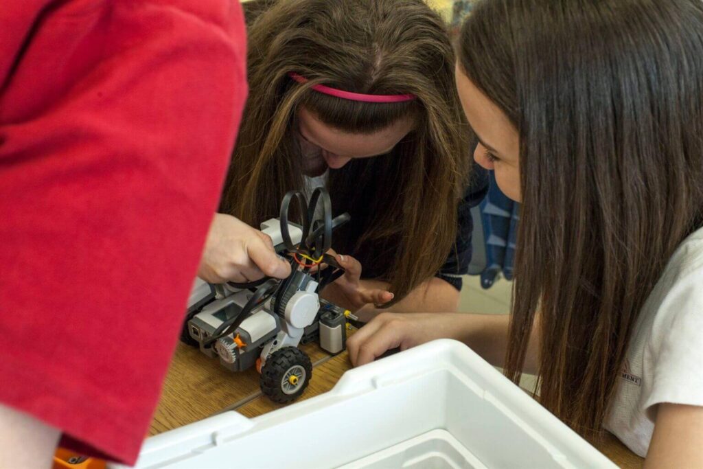 Deux étudiantes assemblant un robot, collaboration et apprentissage, atelier de robotique scolaire, activité pratique, environnement éducatif, concentration sur les détails techniques.