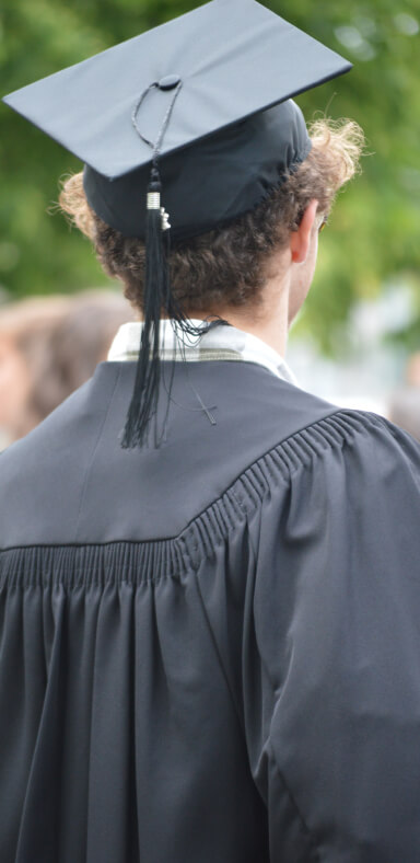 Vue arrière d'un étudiant portant une toge et un mortier noir, cérémonie de graduation, arrière-plan flou, ambiance extérieure, célébration académique, fin d'études, tradition scolaire, réussite, moment mémorable.