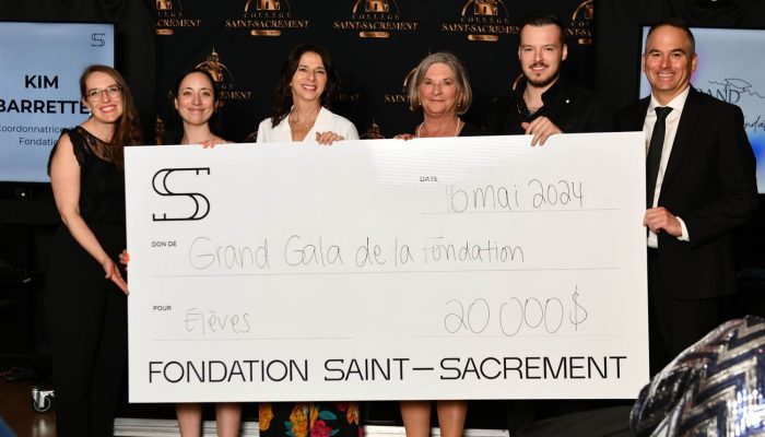 Six membres de la Fondation Saint-Sacrament tenant un grand chèque, montant de 20 000 $, Grand Gala, collecte de fonds, contribution pour les élèves, événement officiel, décor avec logo de la fondation, ambiance professionnelle, solidarité.