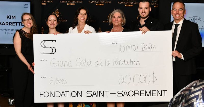 Six membres de la Fondation Saint-Sacrament tenant un grand chèque, montant de 20 000 $, Grand Gala, collecte de fonds, contribution pour les élèves, événement officiel, décor avec logo de la fondation, ambiance professionnelle, solidarité.