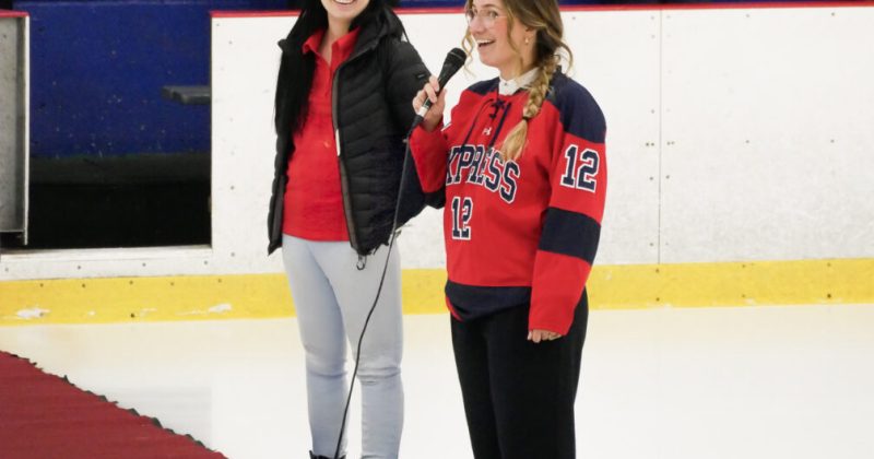 Deux femmes, discours sur la glace, l'une portant un chandail de hockey rouge "Express 12", ambiance sportive, tapis rouge, patinoire, engagement communautaire, Fondation Saint-Sacrament, Collège Saint-Sacrament, spectateurs en arrière-plan.